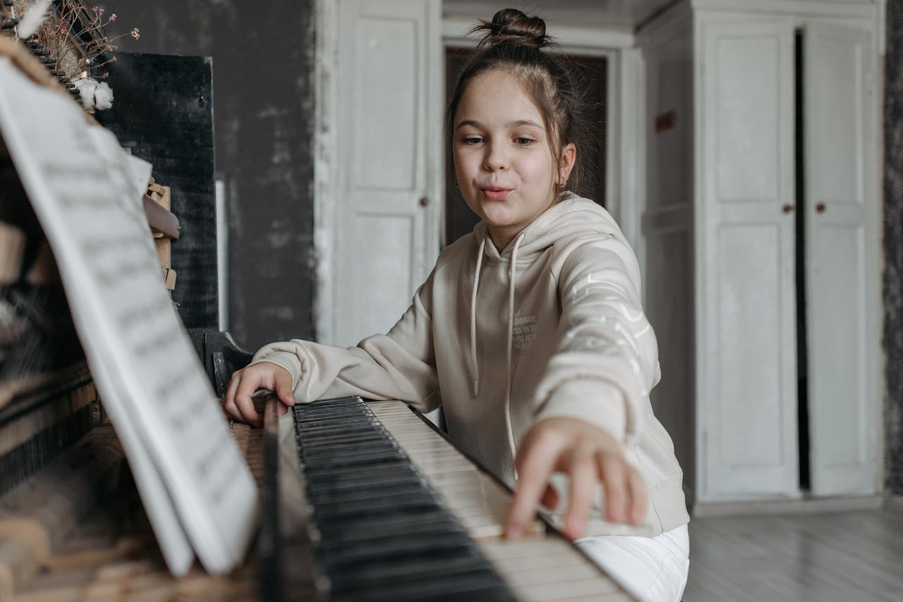 A girl in a beige hoodie practicing piano in an indoor music studio setting.