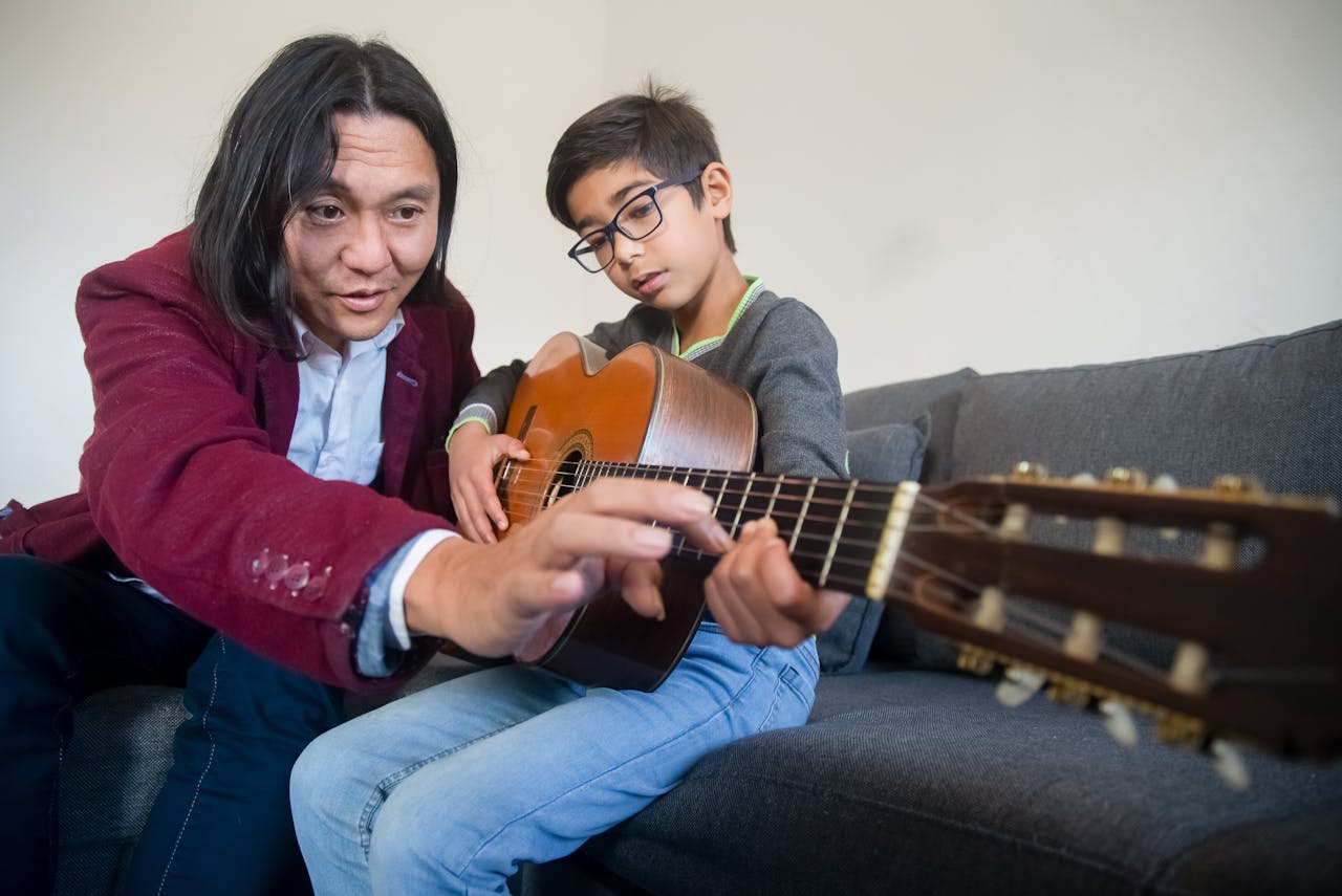 A father tutoring his son on acoustic guitar playing at home, fostering a musical bond.
